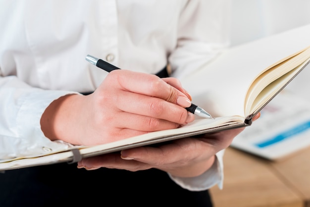 Free photo close-up of businesswoman's hand writing on diary with pen