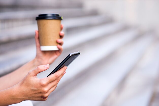 Close up of a businesswoman using mobile phone and holding paper cup. Close-up detail of a businesswoman hand holding paper cup and using a smartphone