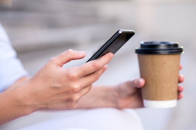 Close up of a businesswoman using mobile phone and holding paper cup. Close-up detail of a businesswoman hand holding paper cup and using a smartphone