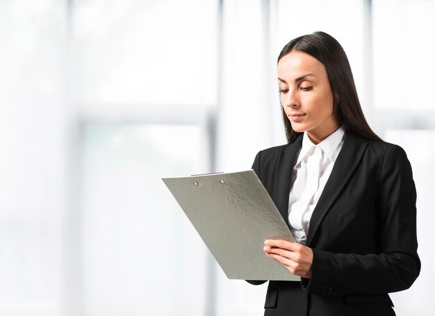 Close-up of a businesswoman writing on clipboard standing near the window