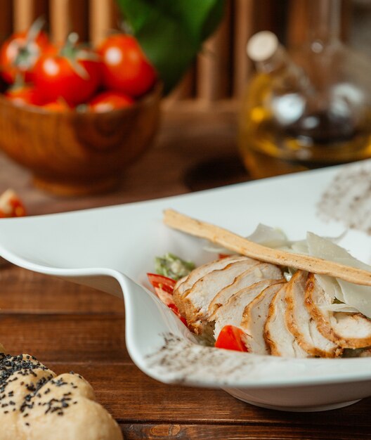 Close up of caesar salad with grilled chicken slices, parmesan and breadstick