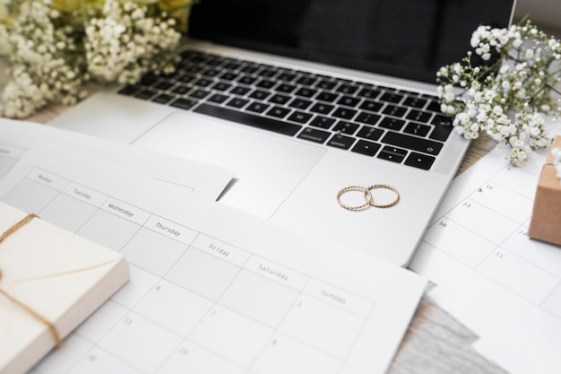 Free photo close-up of calendar; wedding rings; baby's-breath flowers and laptop on desk