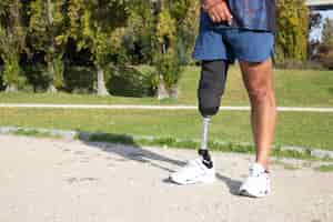 Free photo close-up of caucasian man with mechanical leg. sportsman in blue shorts and white sneakers photographed in park. sport, disability concept