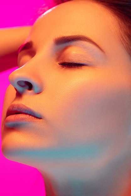 Free photo close up caucasian woman's portrait isolated on pink studio background in mixed neon light. beautiful female model. concept of human emotions, facial expression, sales, ad, fashion. beauty.