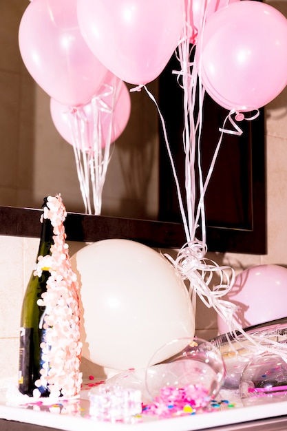 Close-up of champagne bottle with confetti and pink balloons on desk