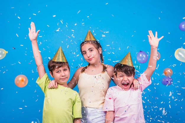 Free photo close-up of cheerful siblings with confetti and balloons over blue backdrop