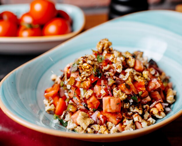 Close up of chopped fresh salad with tomatoes peppers herbs and walnuts in a plate