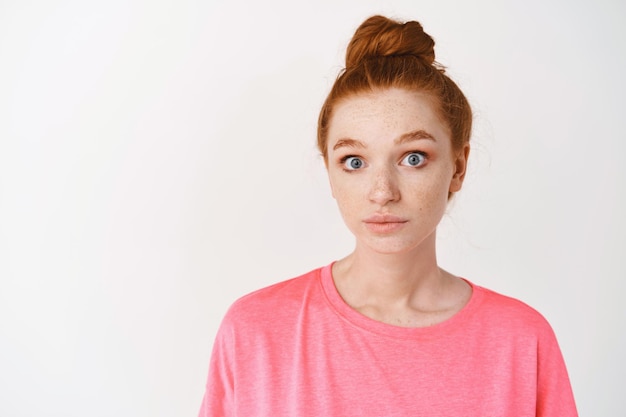 Free Photo close-up of clueless young redhead woman acting confused, staring with blue eyes at front and shrugging, standing over white wall