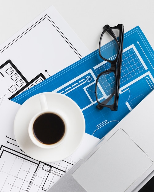 Free photo close-up of coffee cup with blueprints on desk