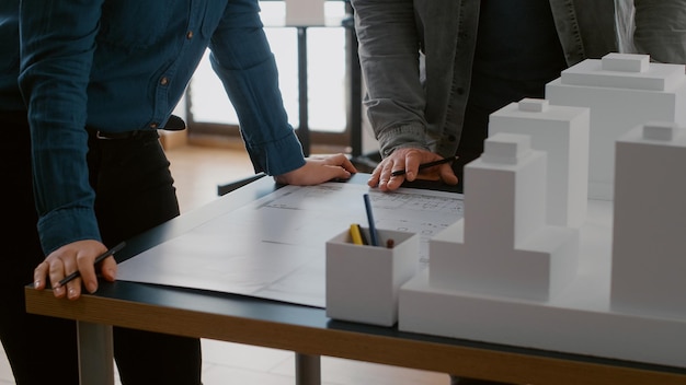 Free Photo close up of colleagues working on urban design with blueprints and building model. team of people doing teamwork on construction layout, designing architectural development project.