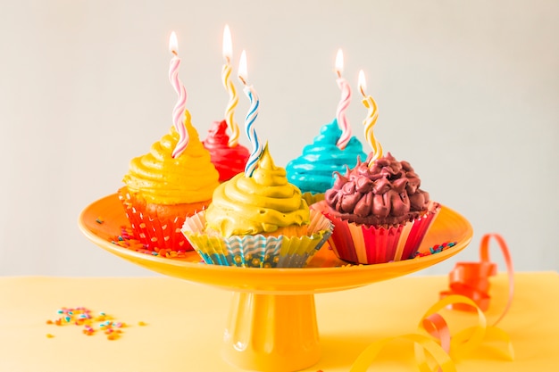 Free photo close-up of colorful muffins with illuminated candles on cakestand