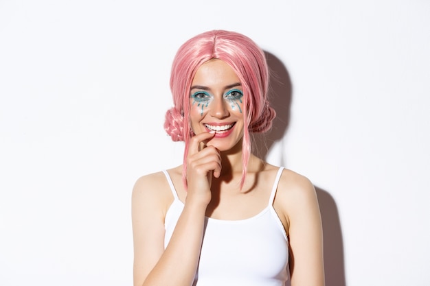 Free photo close-up of coquettish smiling woman in pink party wig, touching lip and looking with temptation, standing.