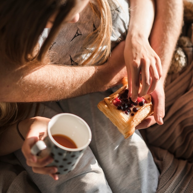 Close-up of couple's hand holding baked pastry and coffee cup