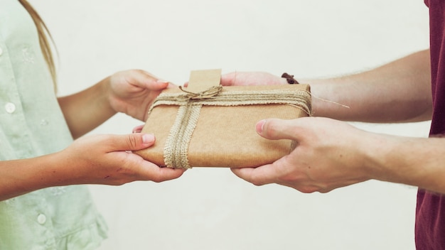 Free photo close-up of couple's hand holding gift in front of plain background