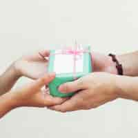 Free photo close-up of couple's hand holding green gift box against plain background