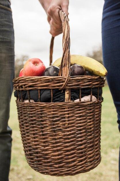 Close-up of couple's hand holding picnic basket full of fruits