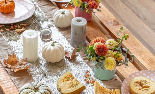 Close-up of cozy decor details of a festive autumn dining table with pumpkins, flowers and candles.