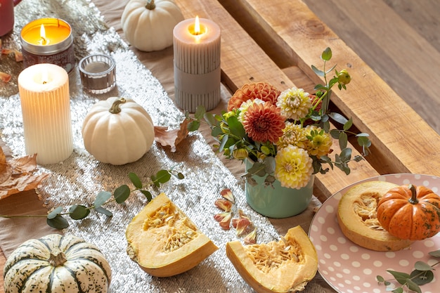 Close-up of cozy decor details of a festive autumn dining table with pumpkins, flowers and candles.