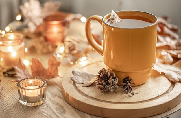 Close-up of a cup of tea among the autumn leaves and candles on a blurred background.