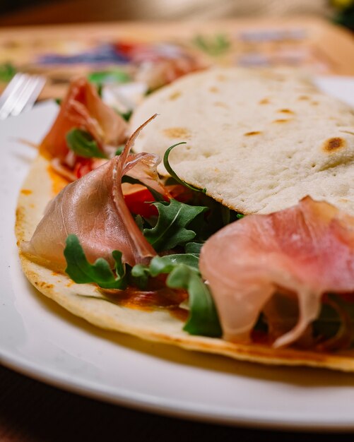 Close up of cured meat wrap with rocket cherry tomato and tomato sauce