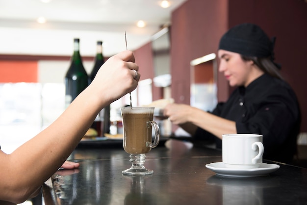 Free Photo close-up of customer at bar counter stirring cocktails in the bar