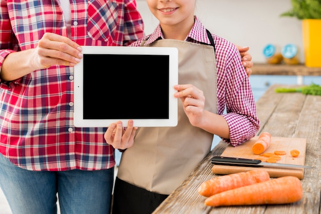 Free Photo close-up of daughter and her mother showing digital tablet with carrot of table