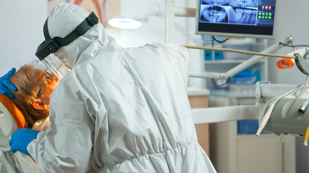 Free photo close up of dentistry doctor in coverall using drilling machine for examining patient during global pandemic. medical team wearing protective suit,, face shield, mask, gloves in stomatological office