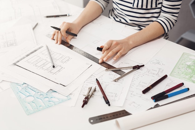 Close up detail of young professional female engineer hands making edits with ruler and liner in new team project. Teamwork and business.