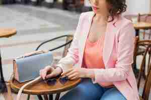 Free photo close up details of accessories of stylish woman sitting in cafe drinking coffee, sunglasses, handbag, spring summer fashion trend, elegant style