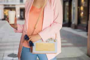 Free photo close up details of accessories of woman in stylish apparel walking in street holding sunglasses, handbag, dressed in pink jacket, drinking coffee, spring summer fashion trend