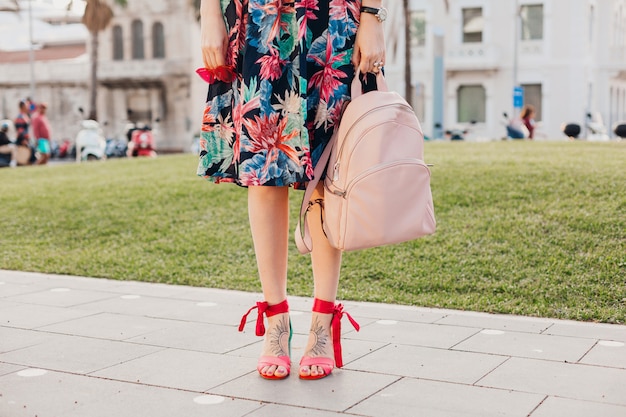 Free photo close up details of legs in pink sandals of stylish woman walking in city street in printed colorful skirt, holding pink leather backpack