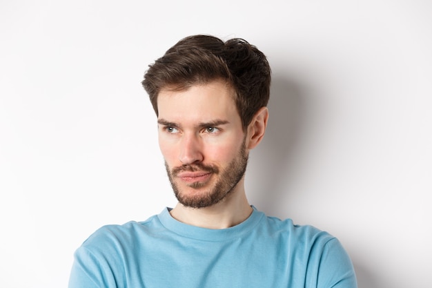 Close-up of disappointed bearded man, sulking and looking left with pensive face, standing upset over white background