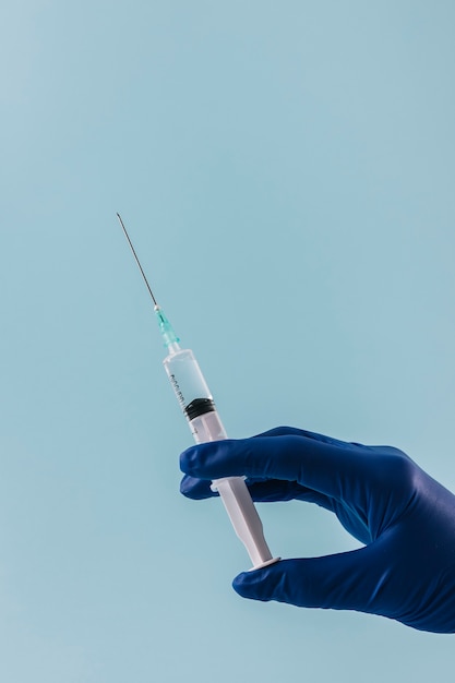 Free Photo close-up of a doctor hand with syringe on blue backdrop