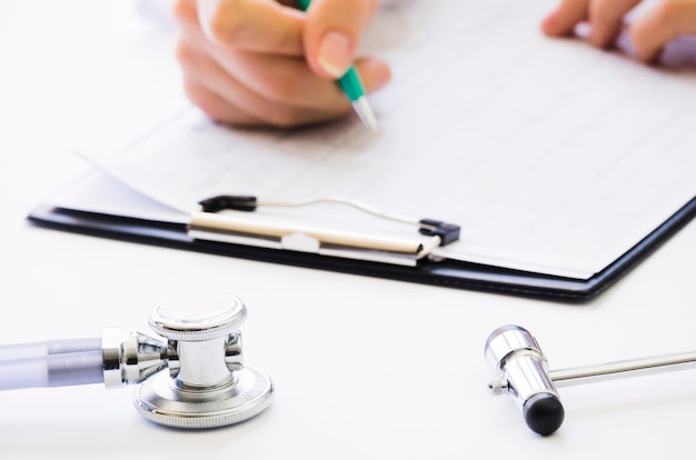 Free photo close-up of doctor's hand holding pen checking the medical report on clipboard