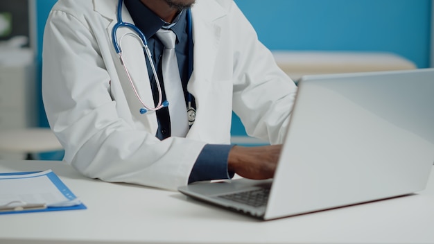 Free photo close up of doctor typing on laptop keyboard in medical cabinet