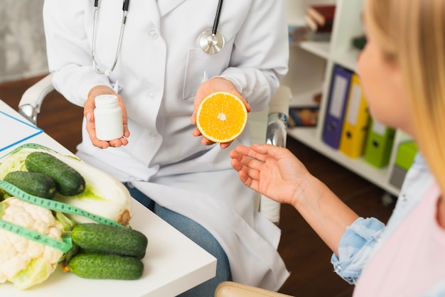 Close-up doctor with pills container and half orange