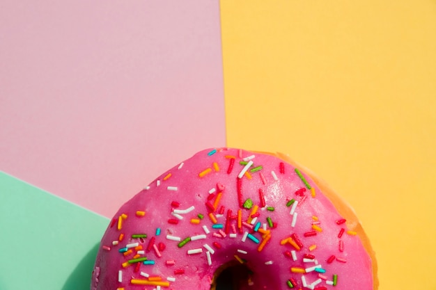 Free photo close-up of donut with sprinkles against yellow; pink; and mint green backdrop