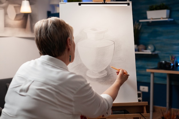 Free Photo close up of elderly woman drawing vase on canvas with pencil