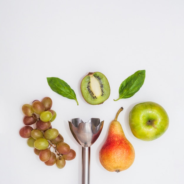 Free Photo close-up of electrical hand mixer with grapes; pears; apple; halved kiwi and basil on white background