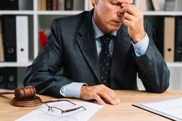 Close-up of exhausted male mature lawyer sitting in front of desk