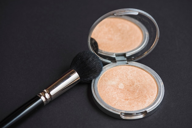 Close-up of face powder and brush on black backdrop