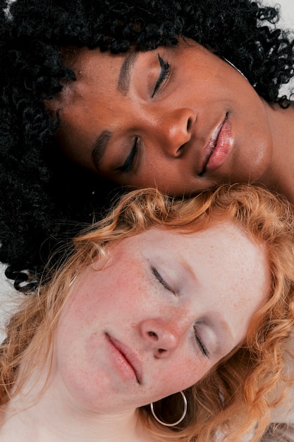 Close-up of fair and dark skinned young woman leaning their head on each other sleeping