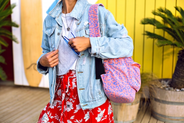 Free Photo close up fashion details of hipster woman wearing bright trendy summer spring clothes, denim jacket, leopard print backpack, floral skirt and casual t-shirt,