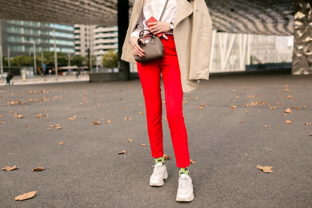 Free photo close up fashion details , young woman wearing trendy red pants funny socks and ugly fashion sneakers, beige elegant coat, posing on the street near business centers, autumn time.