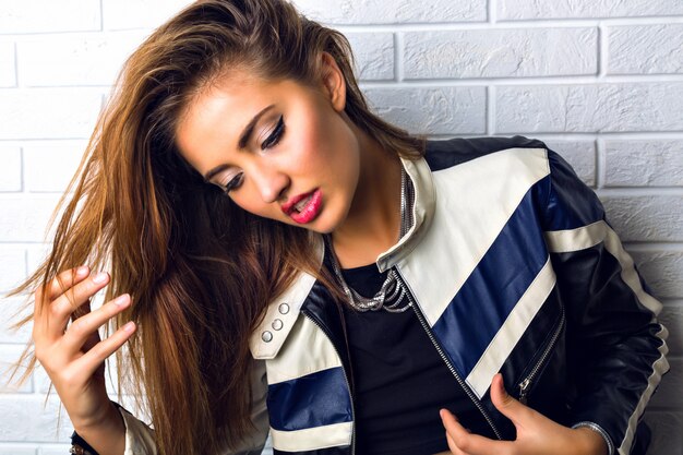 Close up fashion portrait of stunning brunette woman with big blue eyes, full sexy lips and perfect skin, bright glamour make up, wearing biker leather jacket.