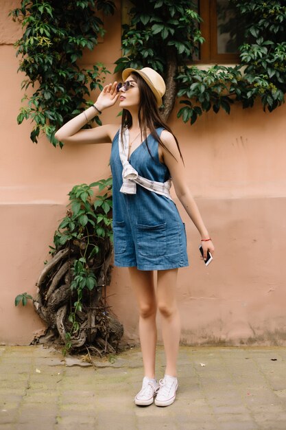 Close-up Fashion woman portrait of young pretty trendy girl posing at the city in Europe,summer street fashion,holding retro fedora hat popular until the 60s.laughing and smiling portrait.trendy