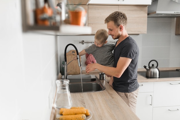 Close-up of a father carrying his son standing near the kitchen sink