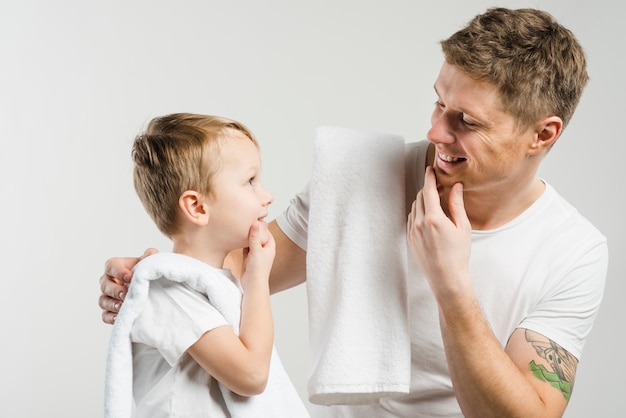 Close-up of father and son touching their chin with hands looking at each other against white backdrop