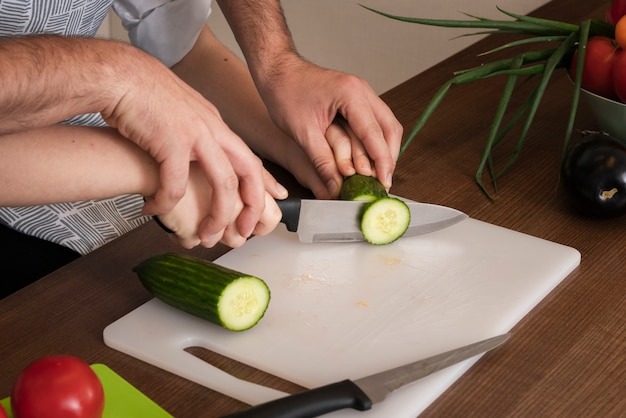 Close-up father teaching son to cut vegetables