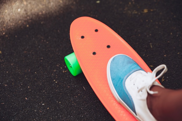 Free photo close up of feet of girl sneakers rides on orange penny skateboard on asphalt